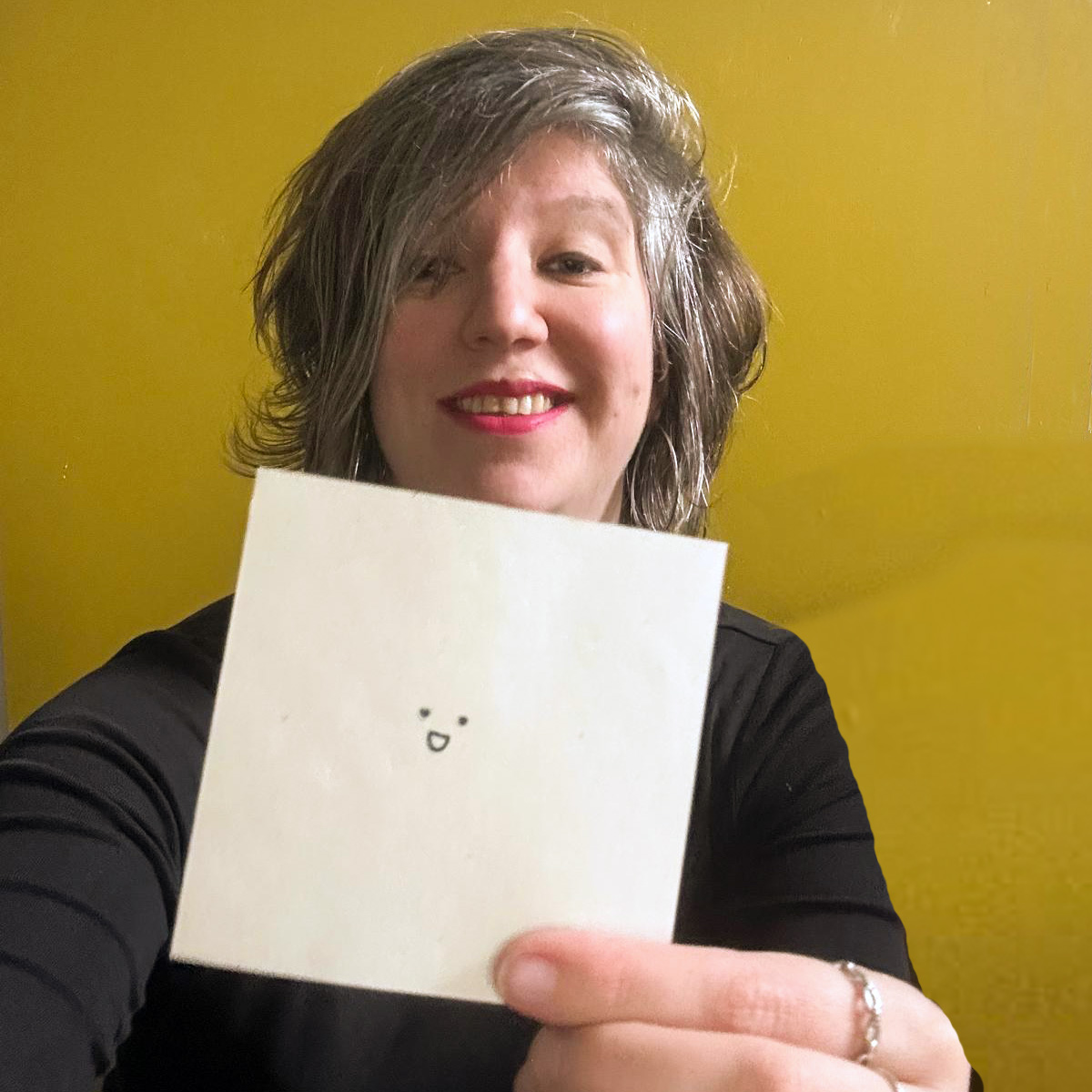 Karin - woordkunstenaar en eigenaar van Taalpracht lachend. Ze houdt een papiertje in haar hand met een lachende smiley erop.